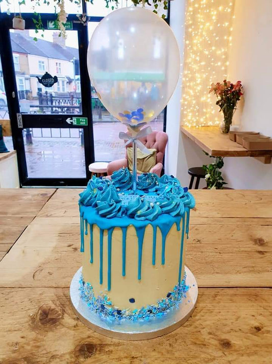 Celebration cake, layered vanilla drip cake topped with a confetti balloon.