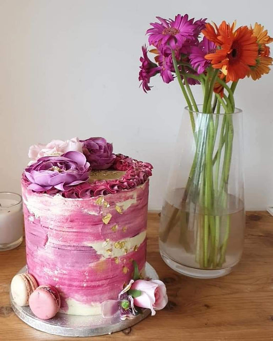 A six inch, four layered three toned textured buttercream cake, topped with flowers, macarons and gold edible leaf.